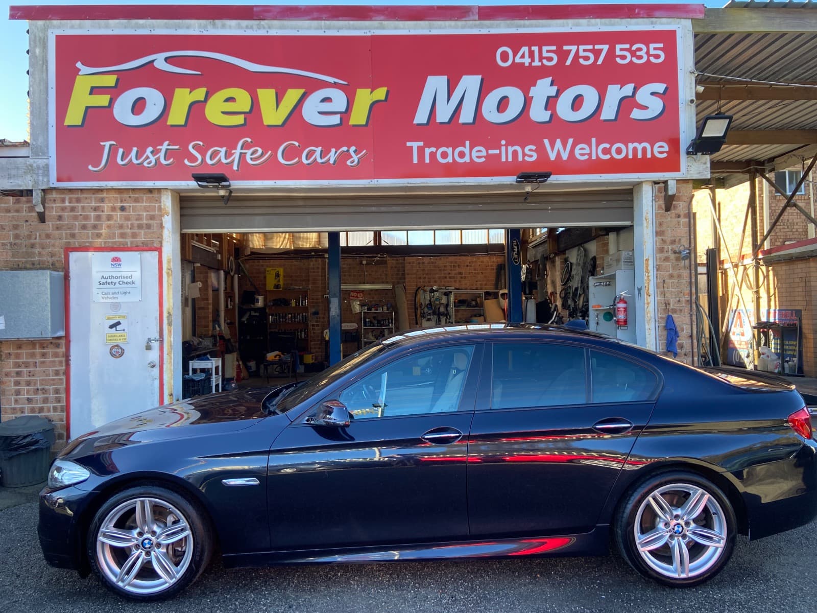 A black BMW sedan parked side-on under the Forever Motors sign, the workshop open behind it